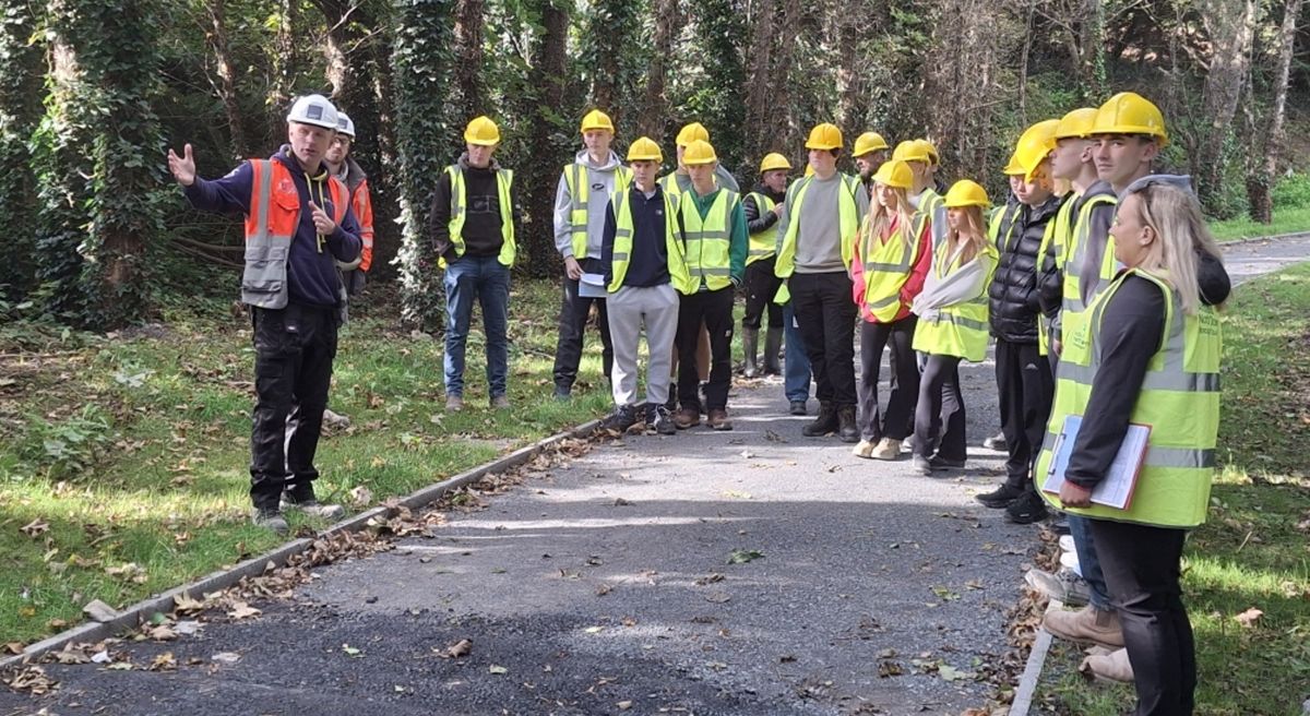 Students in high viz vests and hard hats with contractor on greenway path.