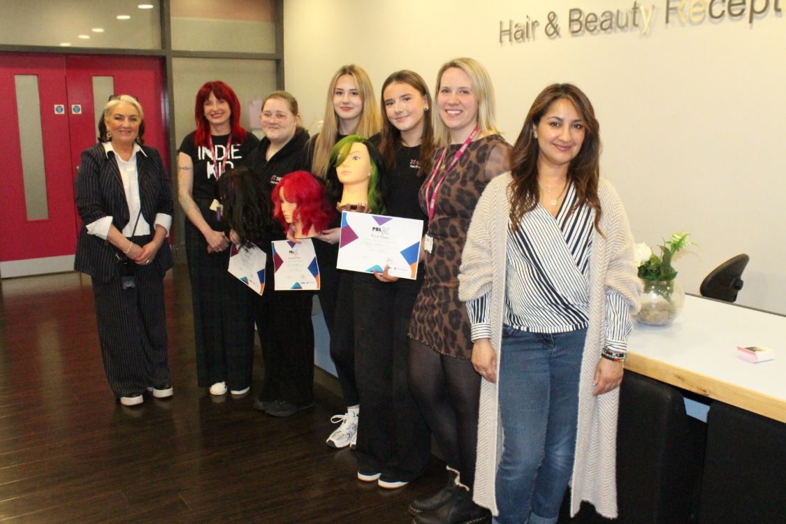 A row of people, some holding certificates and model heads in the reception of the SERC Lisburn Campus salon