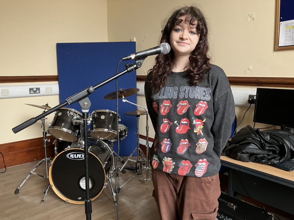 A student at a microphone with musical instruments in the background