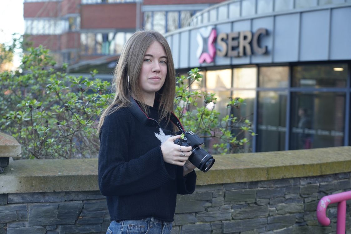 Media student Olyvia Condell, holding a camera, outside SERC Bangor Campus