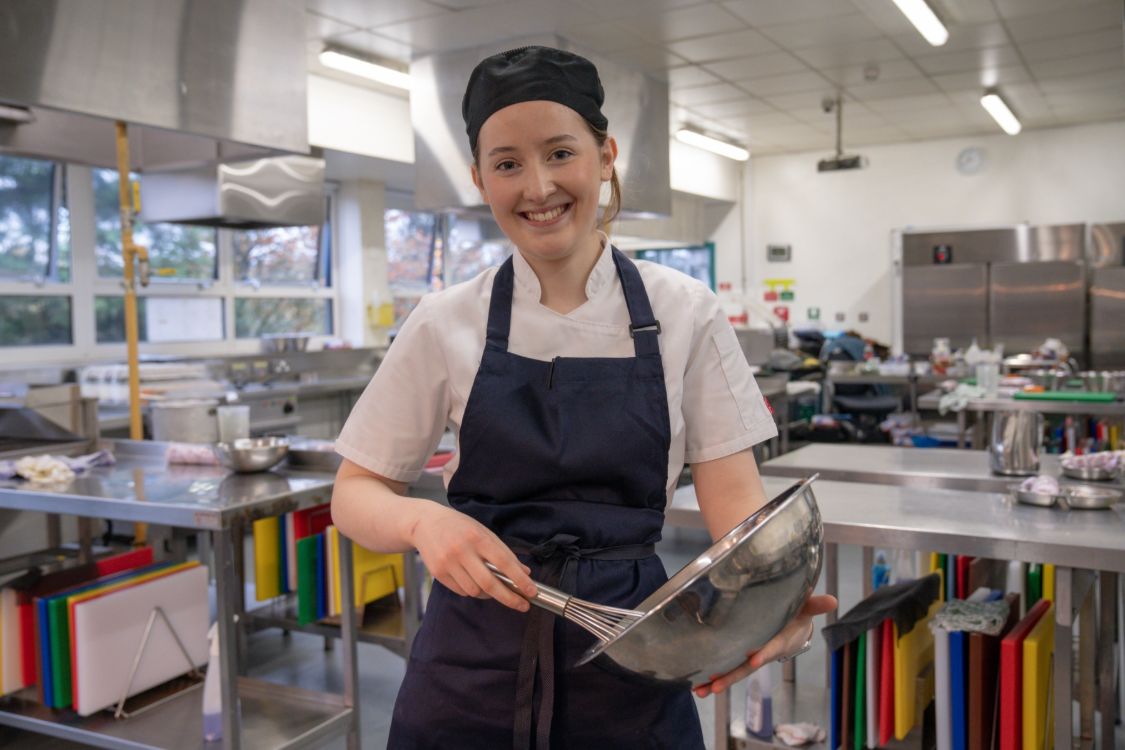 Grace Dugan holding a whisk and bowl in the SERC Bangor Campus training kitchen.