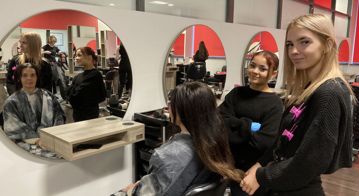 Two hair and beauty students with client in training salon